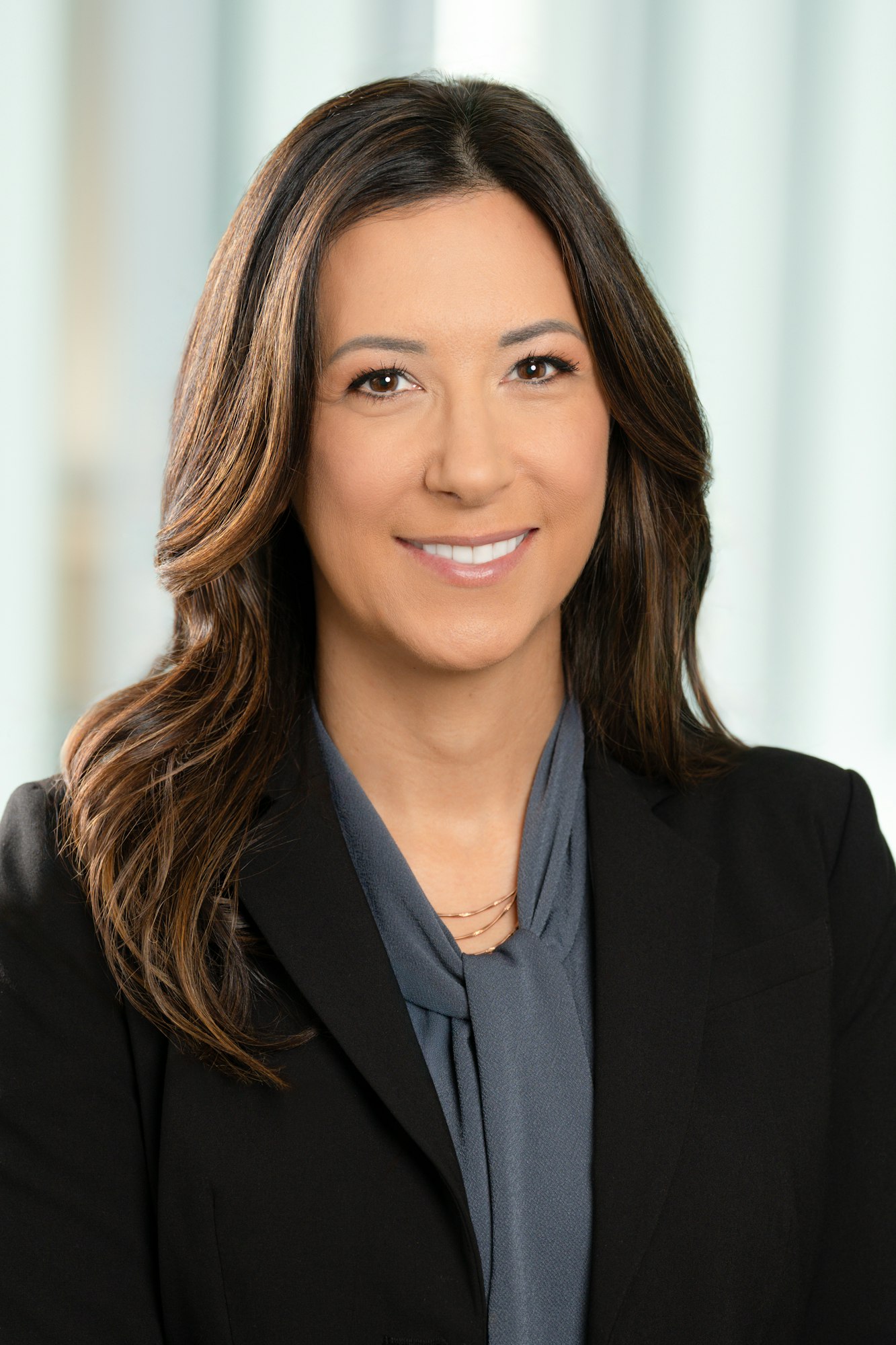 April Wilcox smiling, wearing a black blazer and a gray top, with a blurred background.
