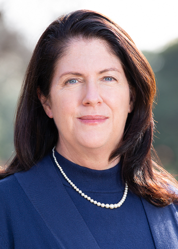 Public Affairs Executive Teresa Schilling has brown hair, wears a blue shirt and pearls.