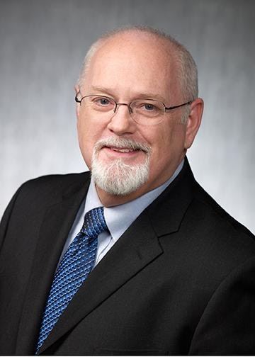 General Counsel Brian J. Bartow wears glasses, a black suit jacket and blue tie.