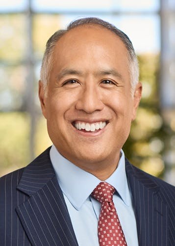 Scott Chan in a suit and tie smiling, with a blurred background.