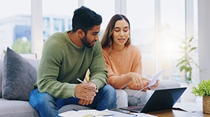 A couple is sitting together, reviewing documents on a laptop in a bright, modern space. They appear engaged and collaborative.