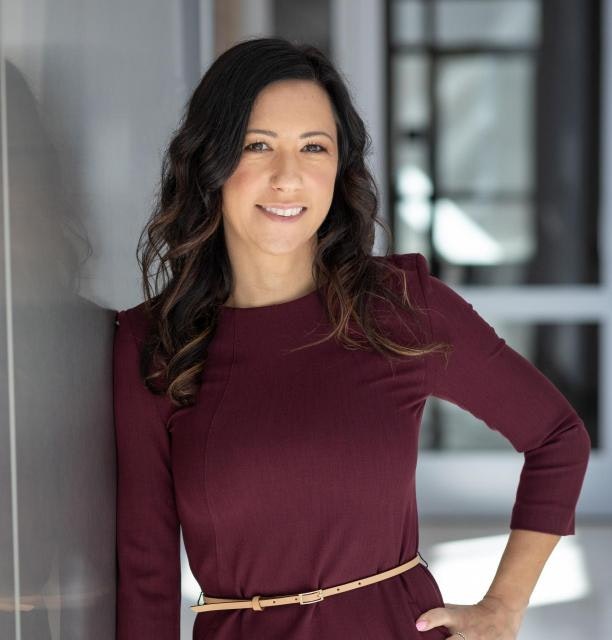 April Wilcox has long brown hair and wears a maroon dress.