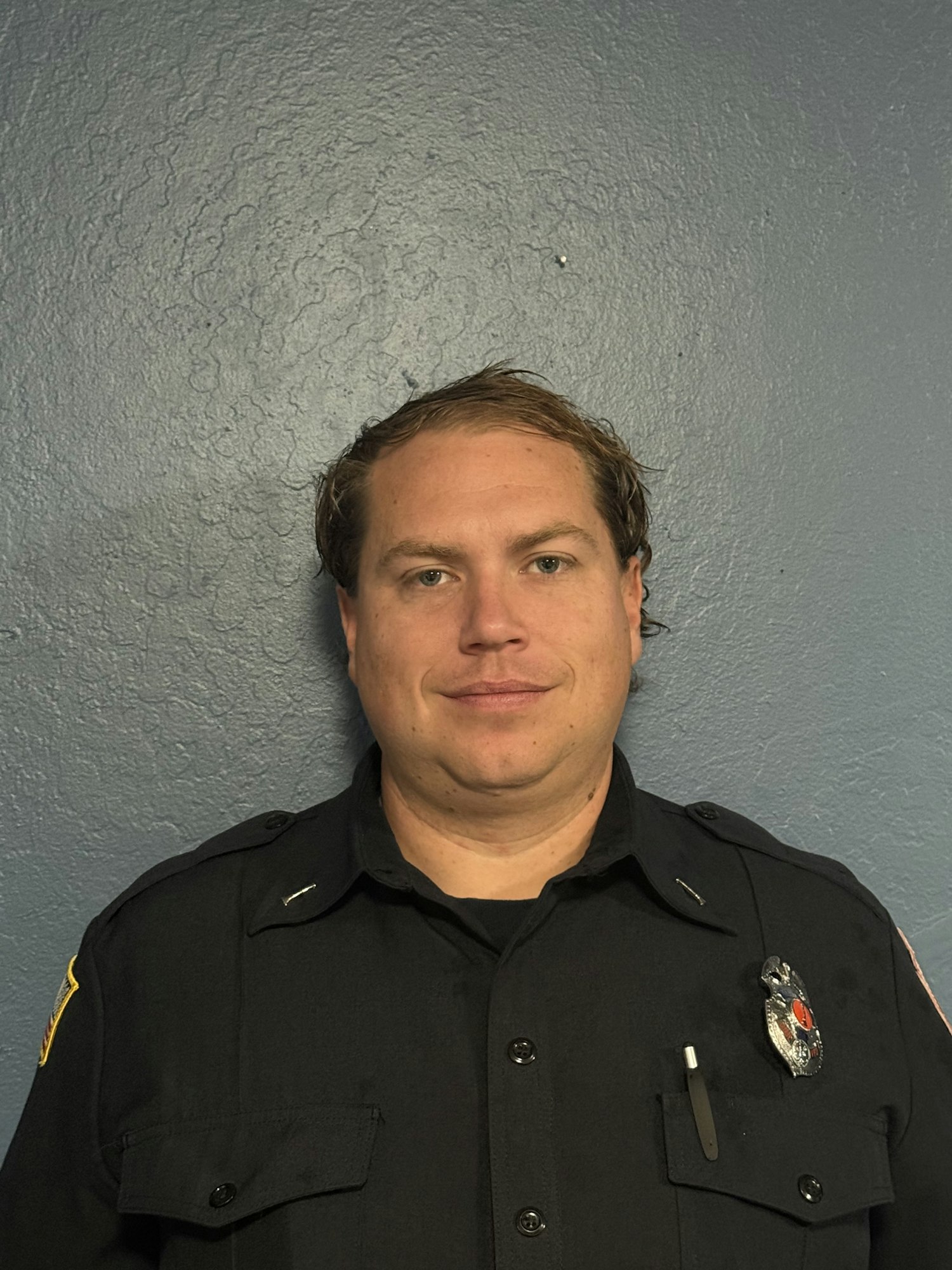A person in a police uniform is lying on the ground with a blue textured wall in the background.