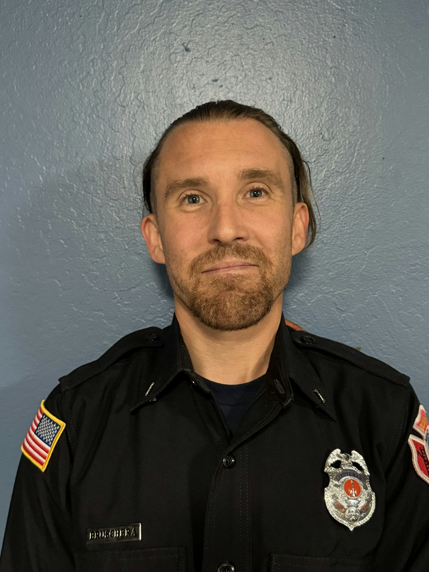 A person in a uniform with a badge, name tag, and American flag patch on the sleeve.