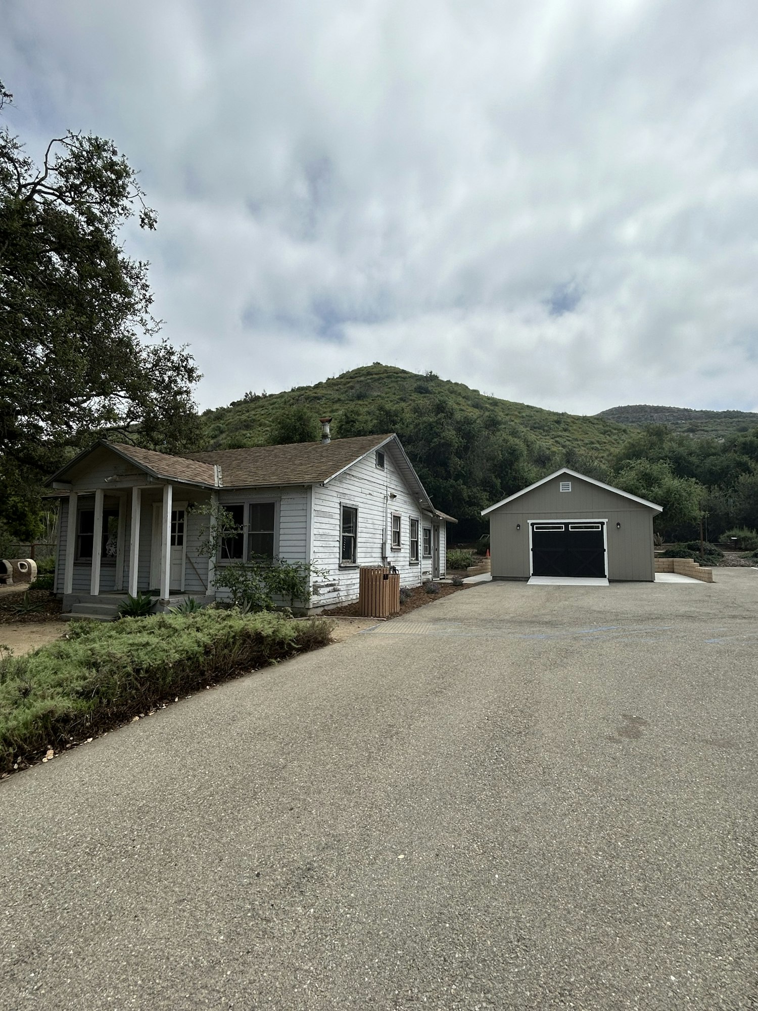 A white house with a porch and detached garage, set against a hilly backdrop with overcast skies.