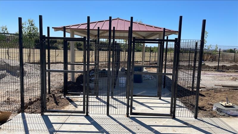 The image shows a fenced area with gate structures, featuring a pavilion in the background and an open landscape.