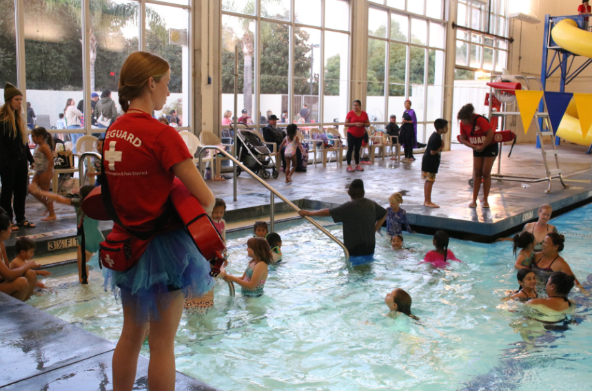 Indoor pool with people swimming and a lifeguard watching.