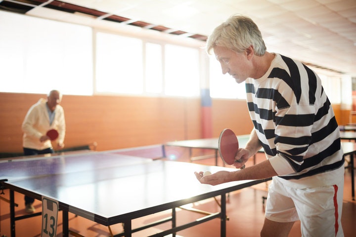 Two older men playing table tennis in a well-lit indoor setting.