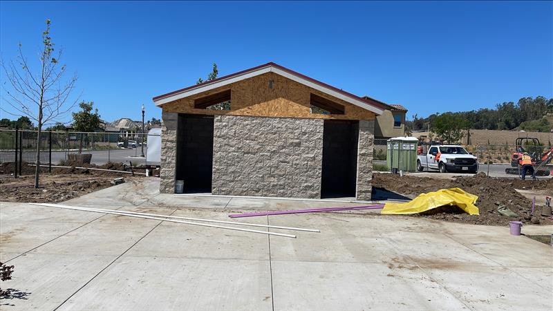 The image shows a partially constructed building with a stone facade, surrounded by construction materials and equipment.