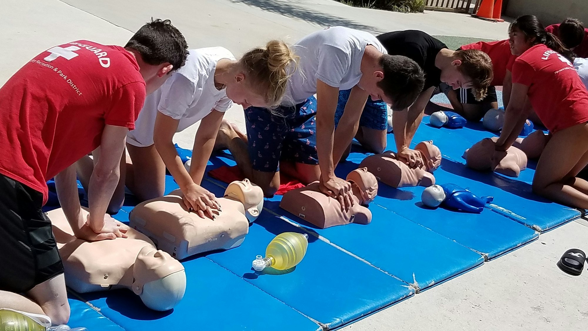 A CPR training session with participants practicing on mannequins outdoors.