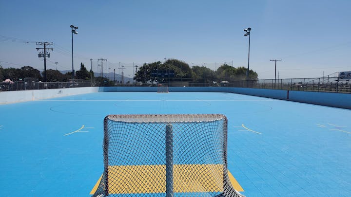 An empty outdoor blue floor hockey rink with nets and surrounding fencing under a clear sky.