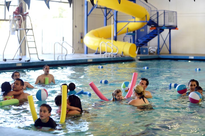 People enjoying a pool with noodles and a water slide in the background.