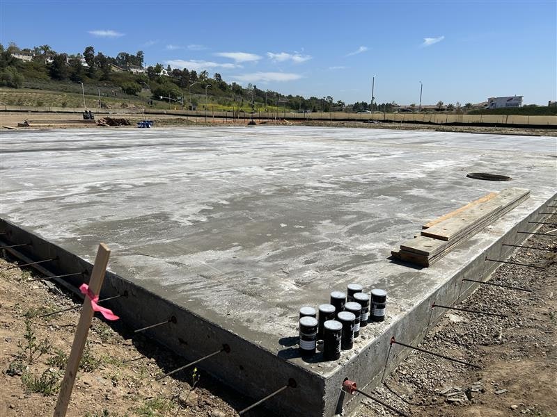 A flat concrete foundation slab under a clear blue sky with some wooden boards and cylindrical objects on the surface.