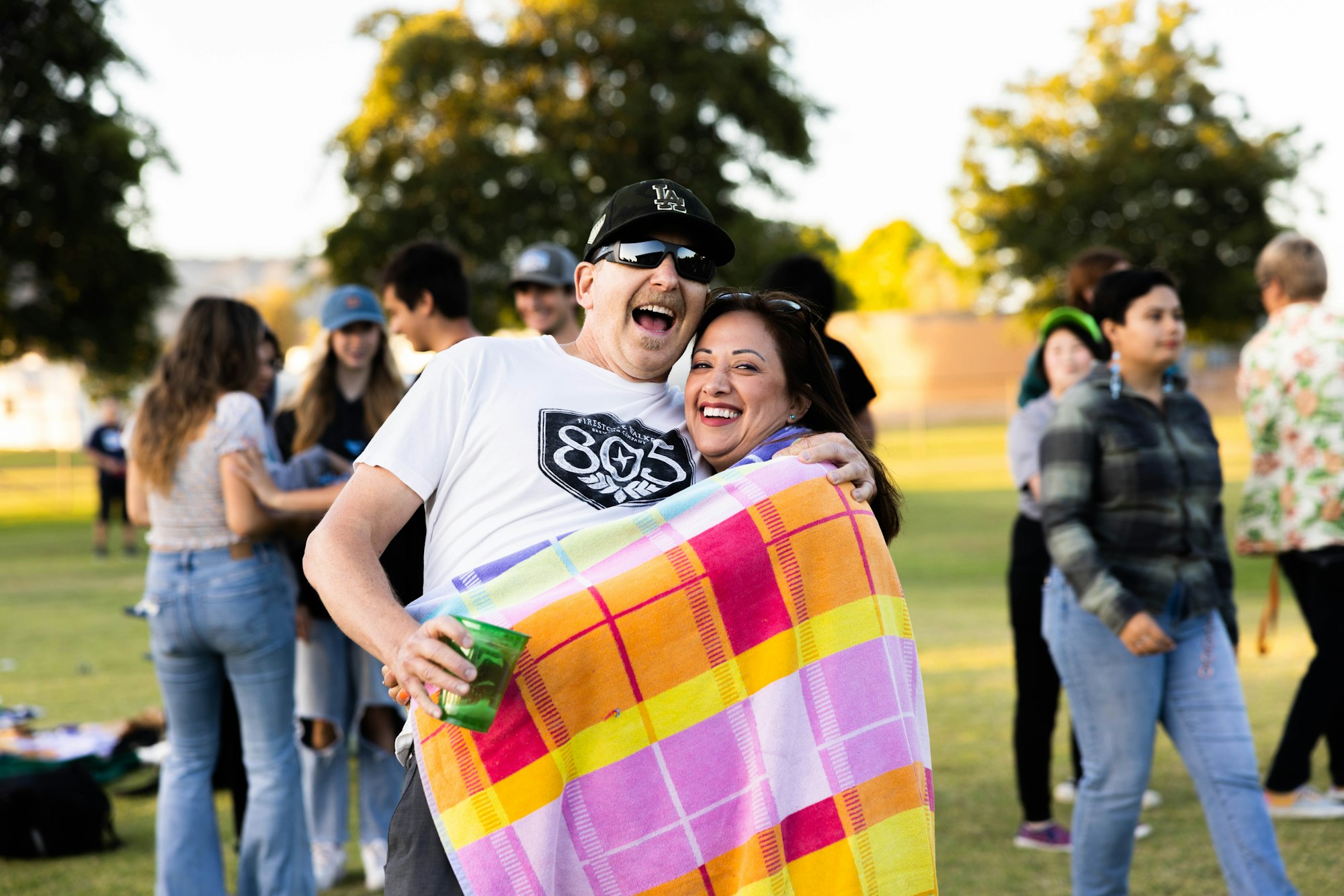 May contain: clothing, pants, grass, nature, outdoors, park, plant, jeans, adult, female, person, woman, head, face, happy, laughing, accessories, glasses, people, t-shirt, hat, photography, portrait, footwear, and shoe