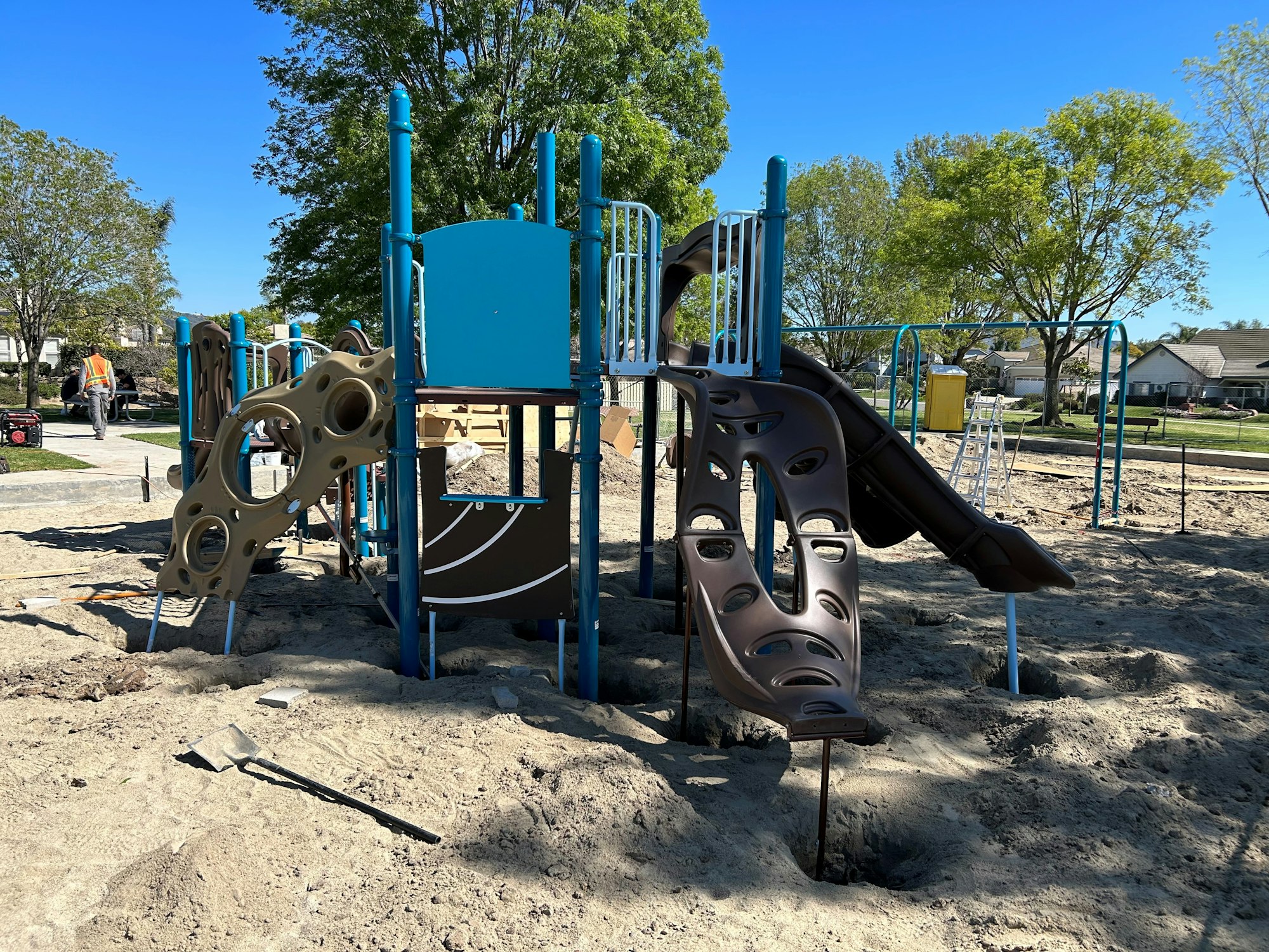 A playground structure under construction with slides and climbing elements in a park setting.