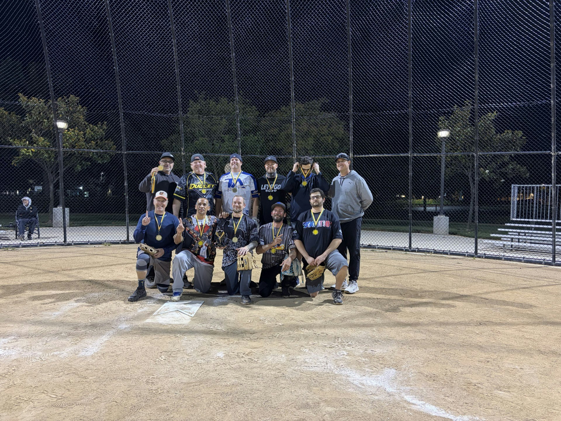 A group of men standing on a baseball field at night, proudly wearing medals and celebrating their achievement.