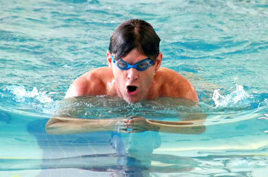 A person swimming breaststroke in a pool, wearing goggles, mid-stroke.