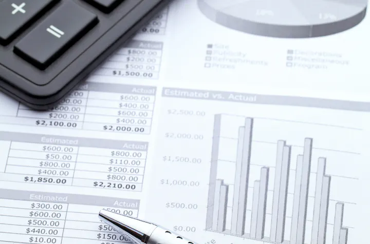 A calculator, pen, and printed financial documents with bar charts and a pie chart, indicating budgeting or accounting work.