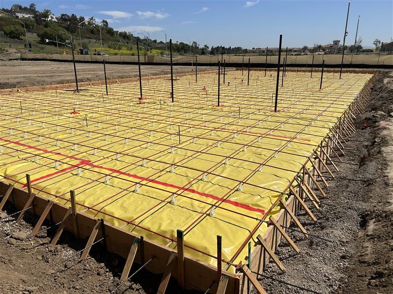 Construction site with a foundation prepared for concrete pouring, featuring rebar and yellow vapor barrier sheets.