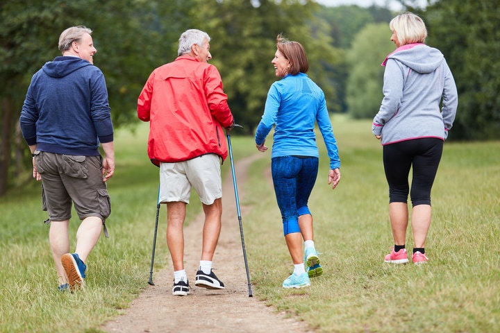 Four people walking outdoors on a path; one uses walking poles.