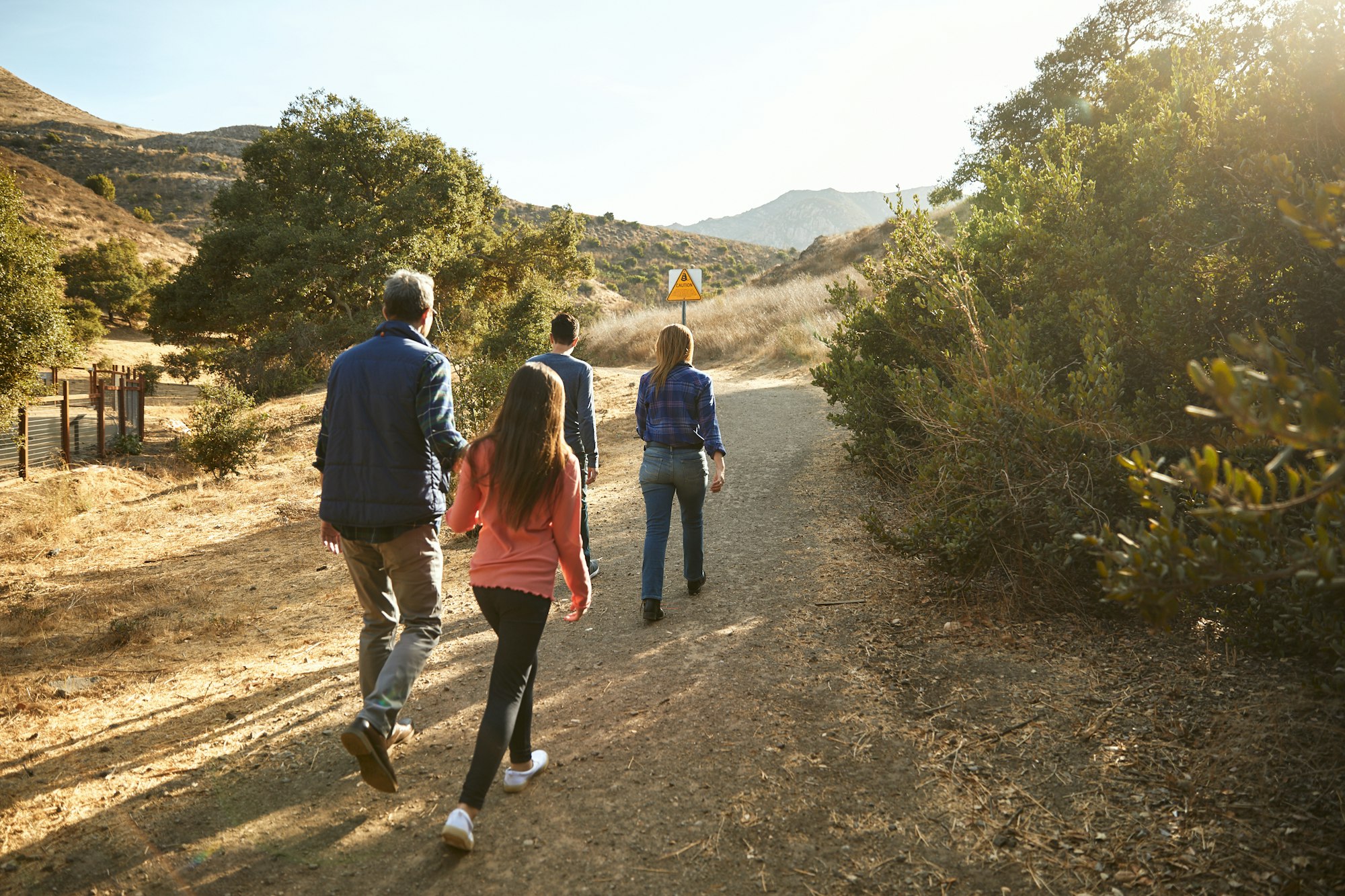 A family of four walking on a sunny nature trail with hills in the background.