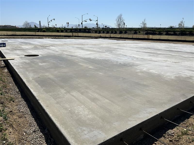 Concrete slab foundation on a construction site with stoplights and trees in the background.
