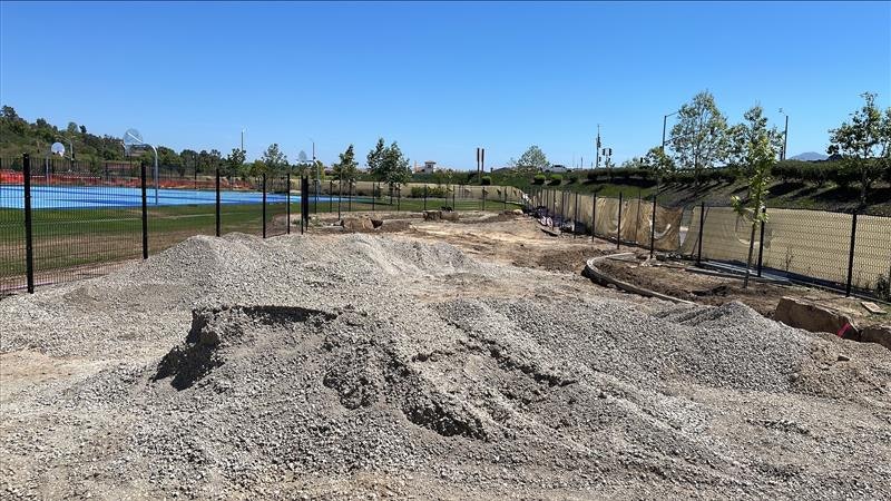 The image shows a construction site with piles of gravel, a fenced area, and a clear blue sky in the background.