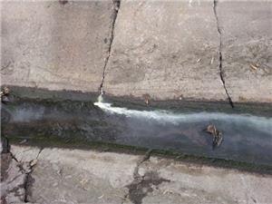 A narrow water stream flowing through a concrete channel with leaves.