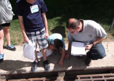 Adult and child examining something on the ground outdoors, with others nearby.