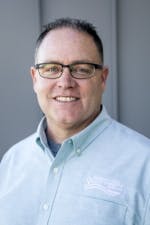 A smiling man wearing glasses and a collared shirt.