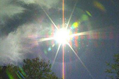 Bright sun with lens flare and clouds, possibly taken through a window given the reflections.