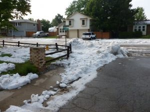 A suburban street with overflowing white foam covering the ground and a wooden fence bordering a driveway.
