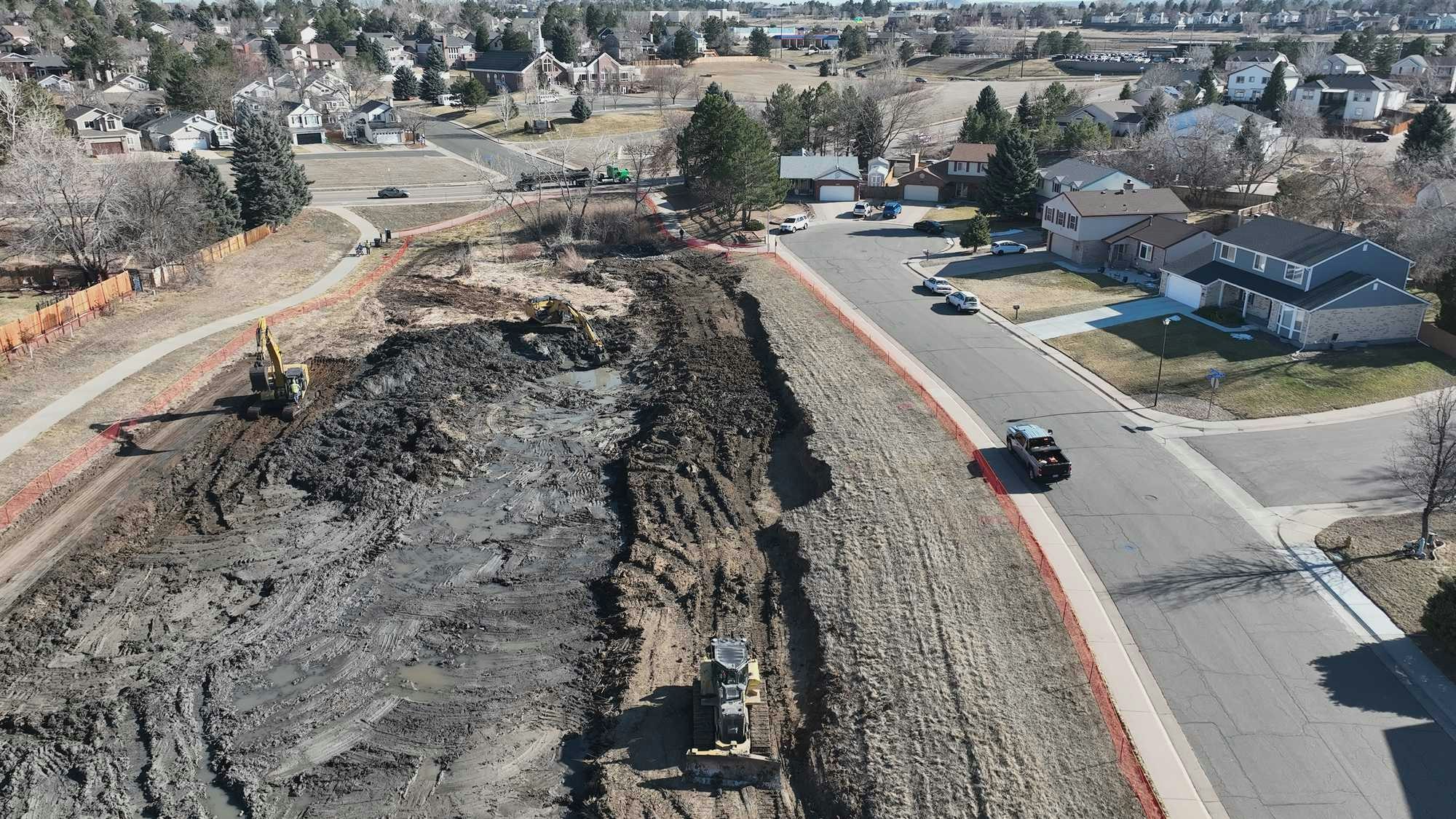 Aerial view of a neighborhood with construction work, excavators, and a muddy site near a residential area.