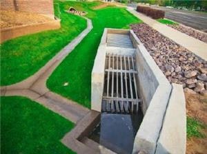 A manicured lawn with a concrete water drainage system and a walking path alongside it.
