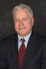 A man in a suit with a red tie on a dark background.