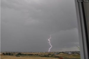 A lightning bolt striking under a stormy sky, viewed from a window.