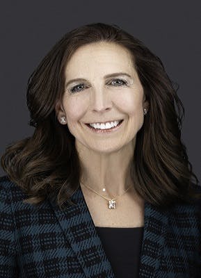 Portrait of a smiling woman with dark hair, a blue jacket, and a necklace.
