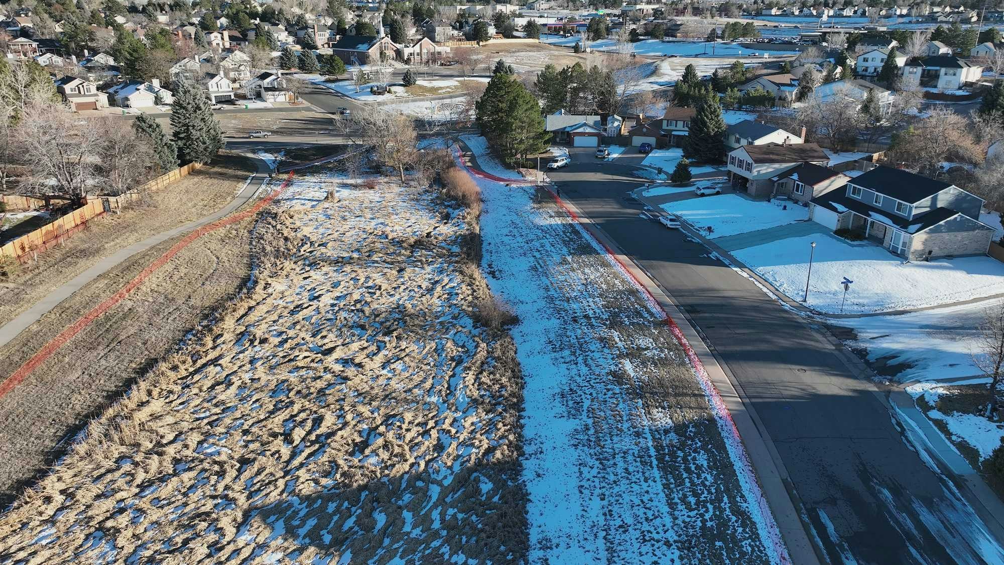 Suburban neighborhood with snow patches, road, houses, trees, and grassy area.