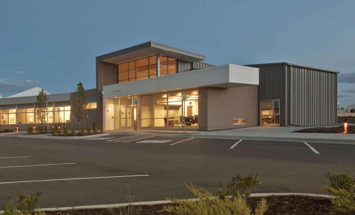 Modern commercial building at twilight with illuminated interior and parking lot.