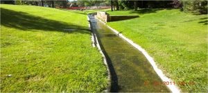 Grassy area with a narrow water channel and stone walls under sunlight.