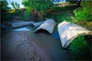 A small stream flowing through concrete culverts with green vegetation around.