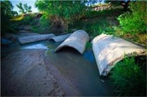 A small stream flowing through concrete culverts with green vegetation around.
