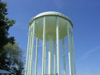 A tall water tower against a clear blue sky, with trees on the left.