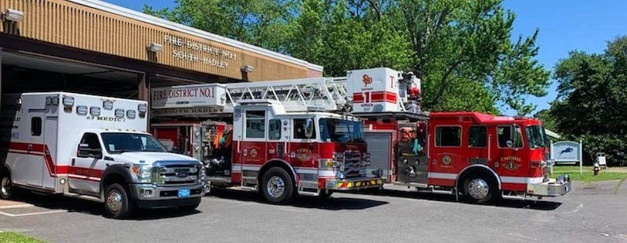 Fire station with an ambulance and two fire trucks parked outside on a sunny day.