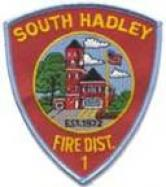 Red shield emblem with "SOUTH HADLEY FIRE DIST." and an illustration of a building, tree, and flag.