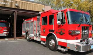A red fire truck parked outside a fire station with another truck partially visible inside.