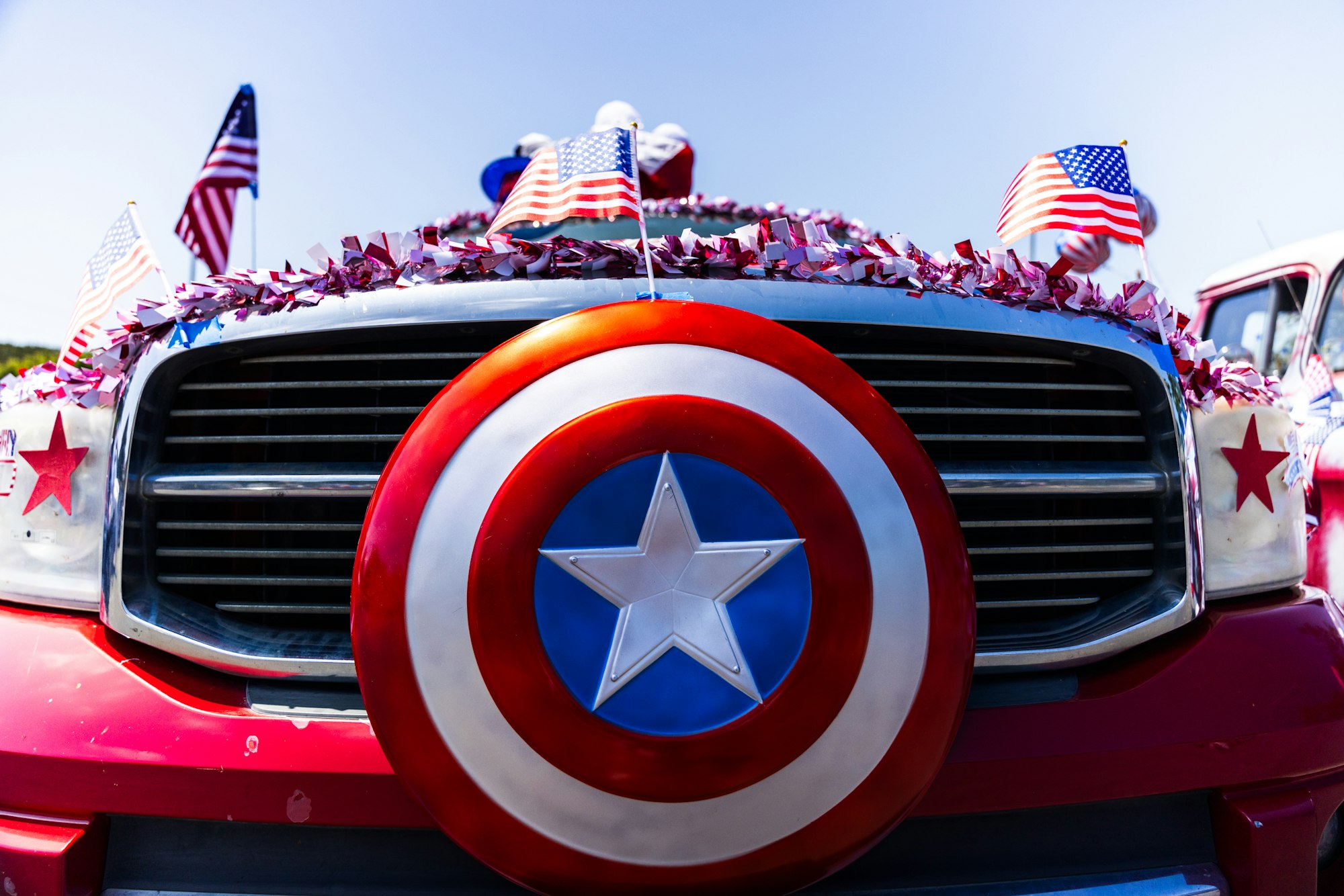 Red vehicle front decorated with a large star shield, American flags, and red tinsel, resembling a patriotic theme.