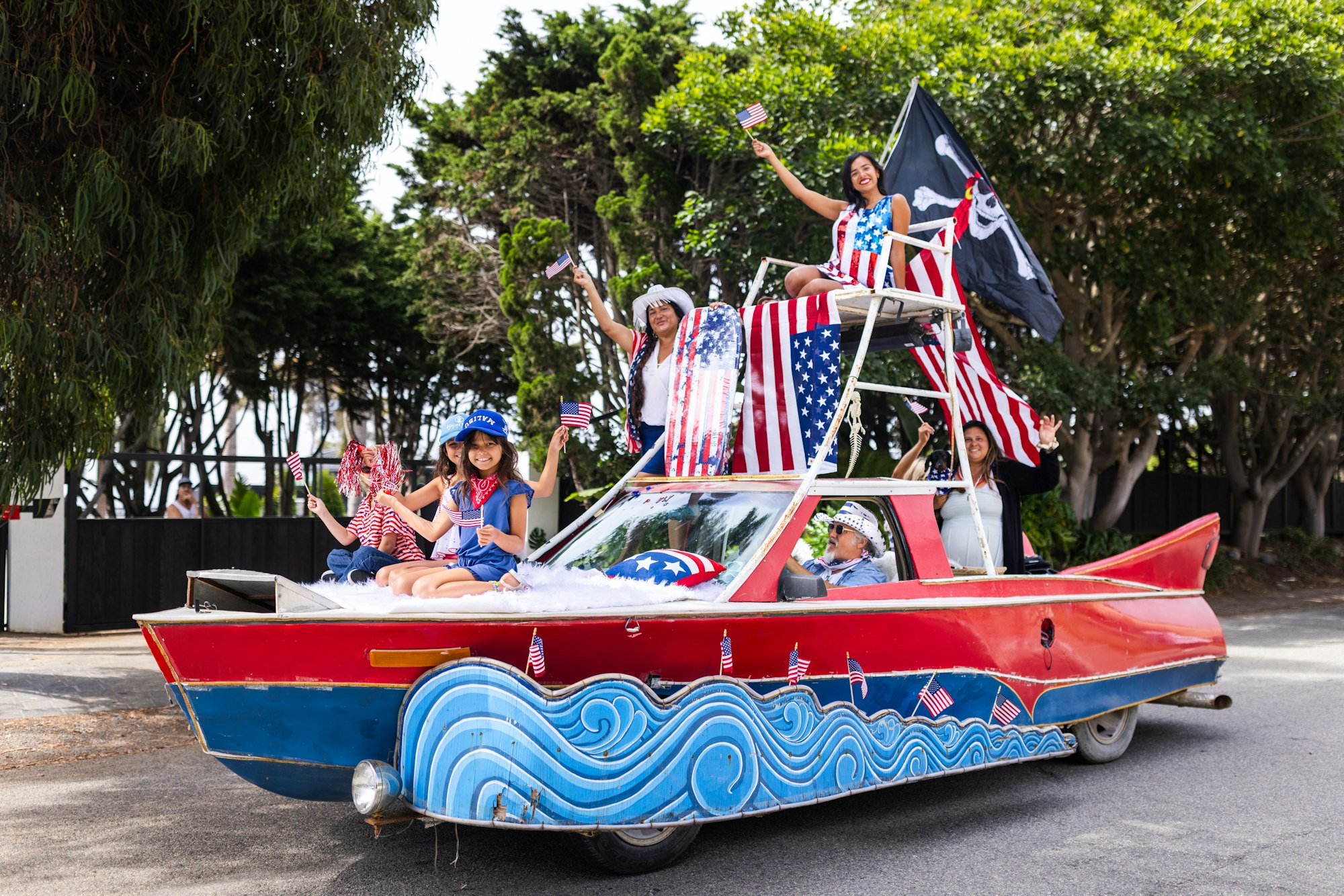 A festive car decorated with American flags, people in patriotic clothing, and a pirate flag, celebrating a holiday.