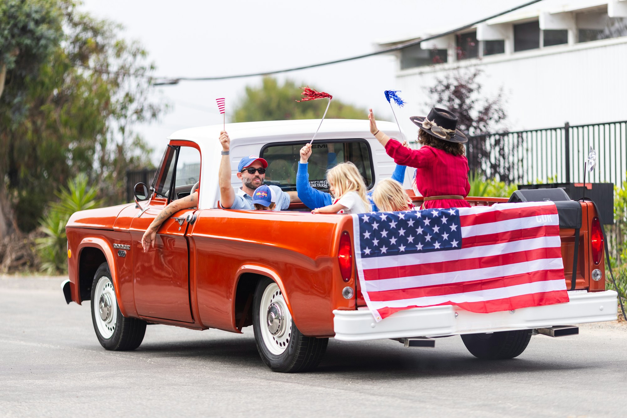 A group of people in a vintage orange truck decorated with an American flag, waving small flags and celebrating.