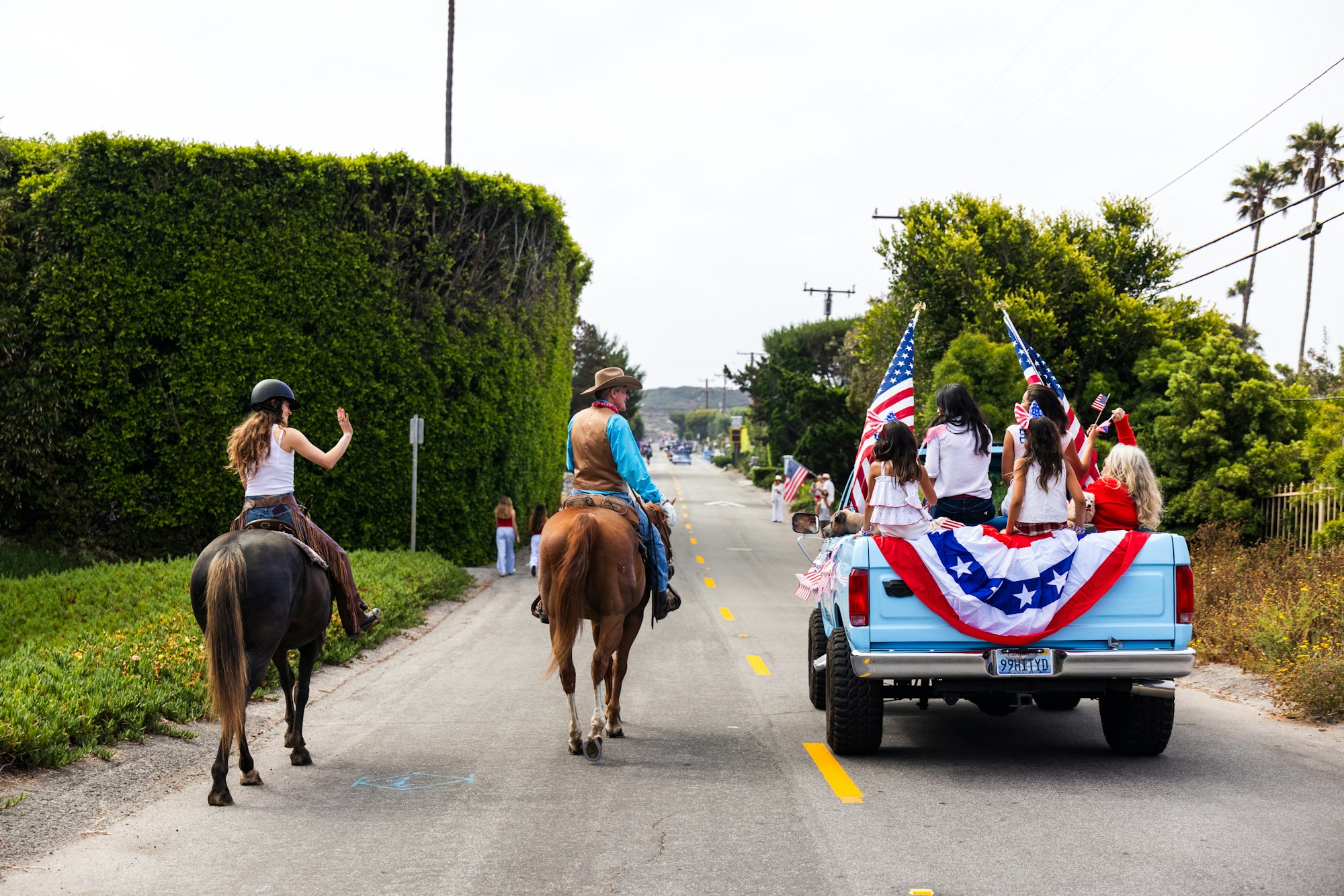 Horses and a truck with American flags on a street, people celebrating.